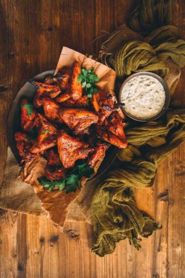 A plate of smoked chicken wings with a dip on a wooden table.